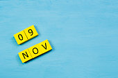 NOV 9, yellow cube calendar on blue wooden surface with copy space