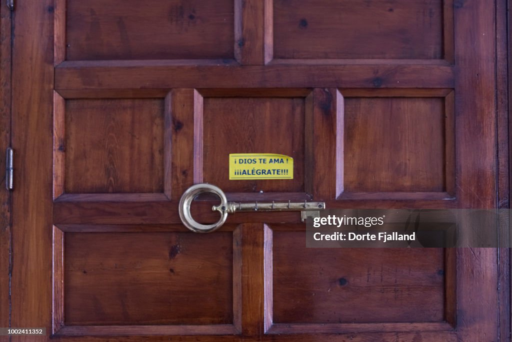 Dark wooden door with a key rack and a sticker with a message in Spanish: "God loves you - Cheer up""