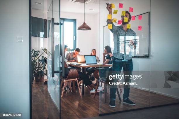 businessman sticking adhesive note on glass wall - jovem empreendedor imagens e fotografias de stock