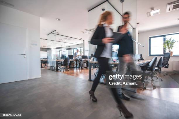colleagues discussing while walking in office - pessoas ao fundo imagens e fotografias de stock