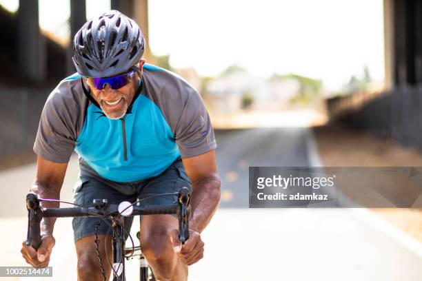 senior black man racing on a road bike - effort stock pictures, royalty-free photos & images
