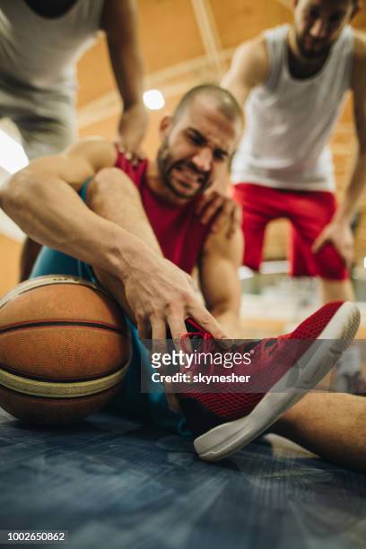 nahaufnahme des verletzten basketballspieler sein bein schmerzen auf dem platz zu halten. - basketball close up stock-fotos und bilder