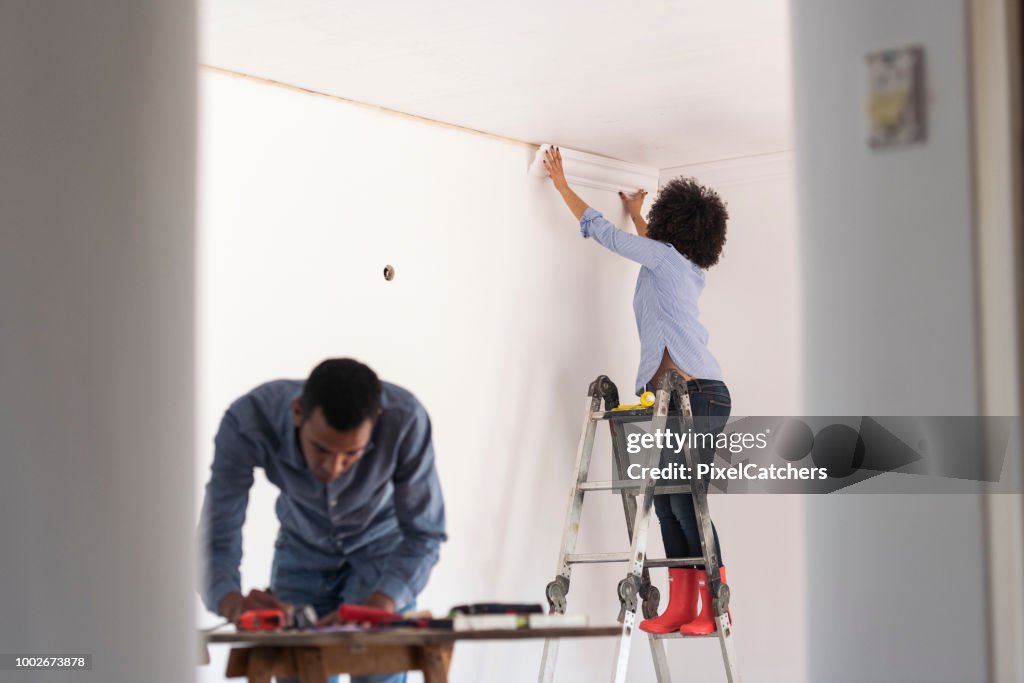 Young woman sticks cornice while young man works on plans on table home renovations