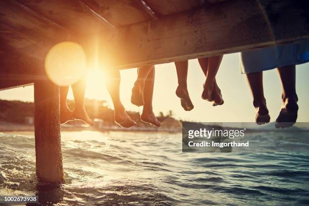 familia sentado en el muelle junto al mar - luz del sol fotografías e imágenes de stock