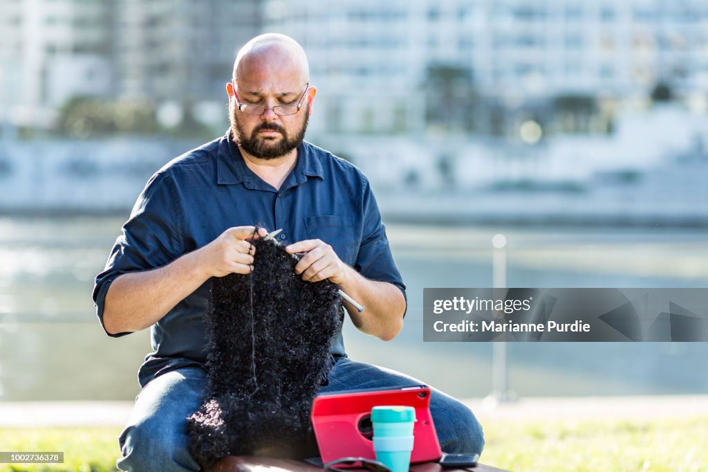 A man sitting on a park bench knitting