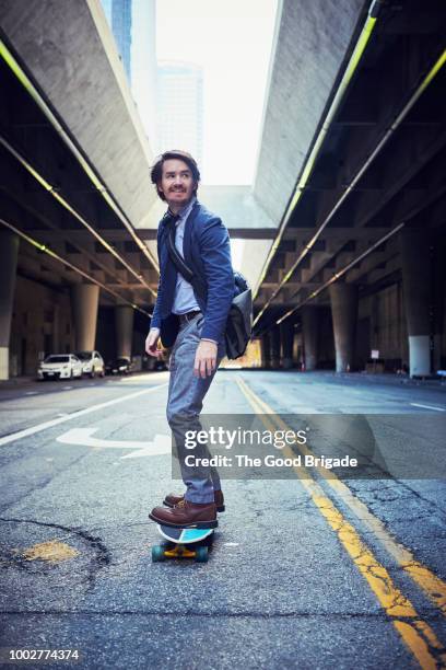 businessman riding skateboard on city street - messenger bag stock pictures, royalty-free photos & images