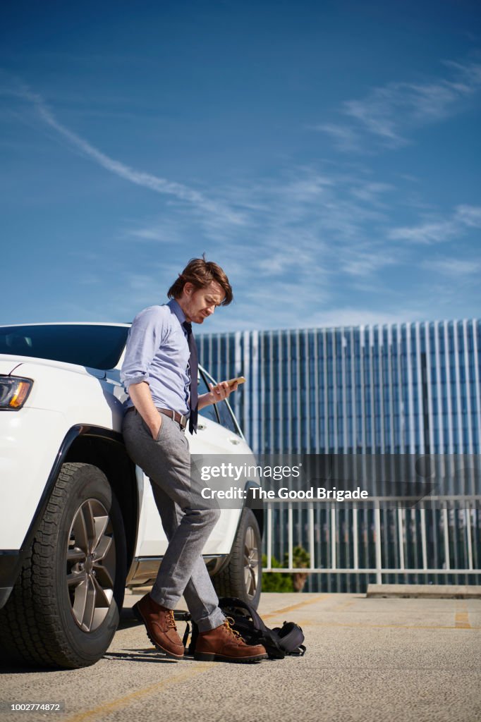 Businessman leaning against car looking at mobile phone