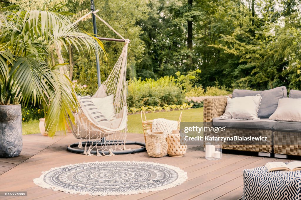 Pillows on hammock on terrace with round rug and rattan sofa in the garden. Real photo