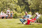 Smiling man with beer talking with friend while relaxing on sunbeds in the garden. Real photo