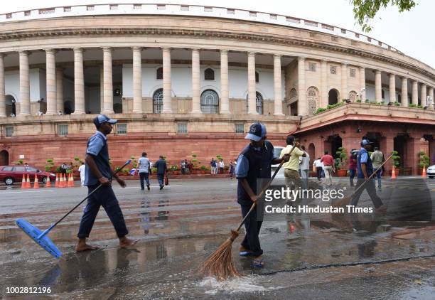 Workers sweep a water-logged area due to heavy rainfall in the national capital in front of Parliament House building during the third day of the...