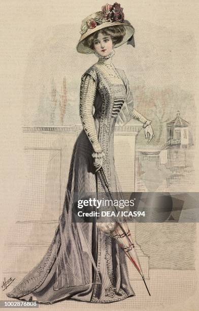 Woman wearing a blue-grey fabric dress with silk embroidery, tulle blouse with pleats and a hat with flowers, creation by Maison Riva, colored...
