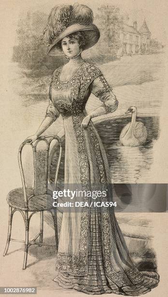 Woman wearing an elegant summer dress in white fine linen or foulard, lace inserts and a hat with feathers, creation by Mademoiselle Louise Piret,...