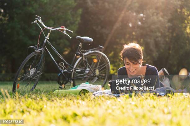 young adult woman reading an ebook at a public park - e reader stock pictures, royalty-free photos & images