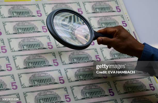 An employee examines a sheet of 5 USD notes as it comes off the printing machine at the US Treasury's Bureau of Engraving and Printing in Washington,...