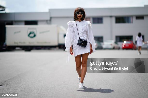 Guest wears sunglasses, a white dress, a Chanel bag, white sneakers , during Feeric Fashion Week 2018, on July 20, 2018 in Sibiu, Romania.