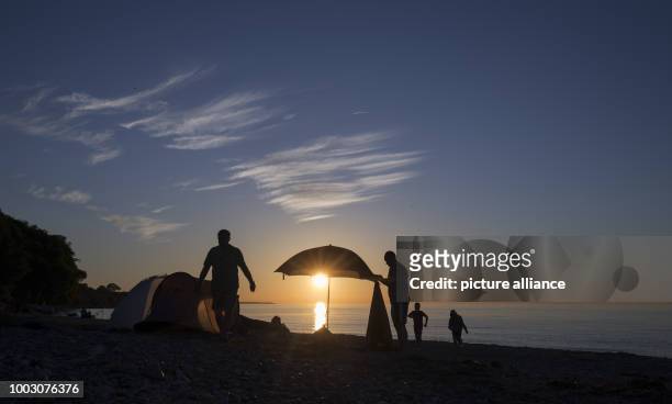 Mit Strandmuscheln und Sonnenschirm ausgestattet ist eine Familie am am Ostseestrand nahe Weißenhäuser Strand im Licht der untergehenden Sonne zu...