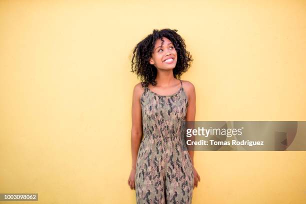 smiling young woman with curly hair standing in front of yellow wall - woman looking up stock-fotos und bilder