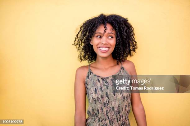 Smiling young woman with curly hair standing in front of yellow wall