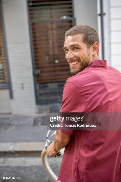 portrait of smiling young man with bicycle on city street turning round - terugkijken stockfoto's en -beelden