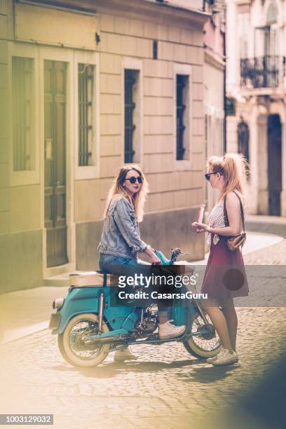 junge frauen treffen auf stadtstraße und reden - holiday scooter stock-fotos und bilder