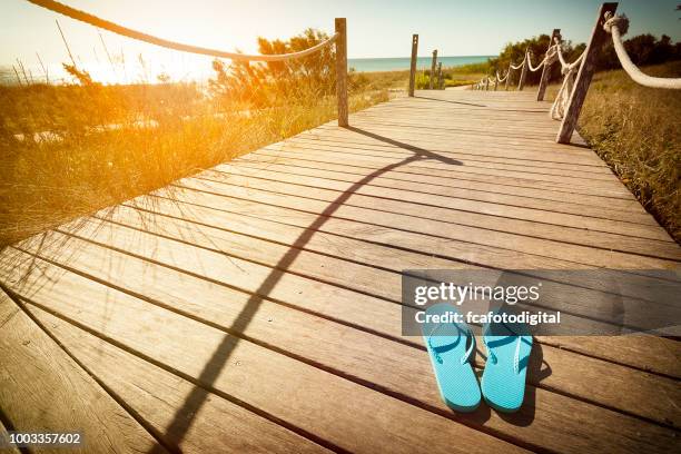 flip-flops auf einem hölzernen fußweg zum strand in den dünen bei sonnenuntergang - beach fence stock-fotos und bilder