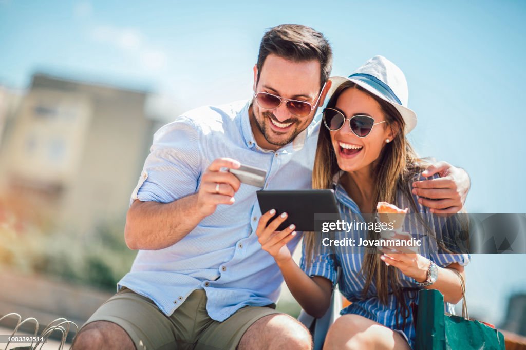 Happy couple paying on line with credit card and digital tablet on the street