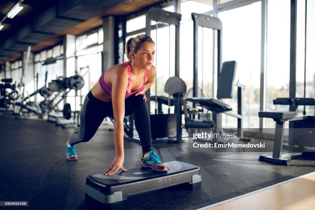 Mujer haciendo estocadas en el equipo de gimnasia de paso en el gimnasio