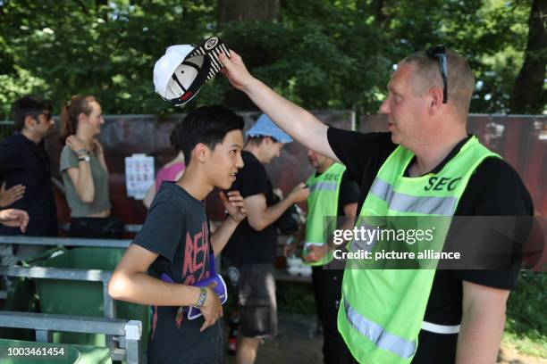 An employee of a security agency checks under neath a hat of a visitor of Rock im Park at the entrance controls in front of the festival grounds in...