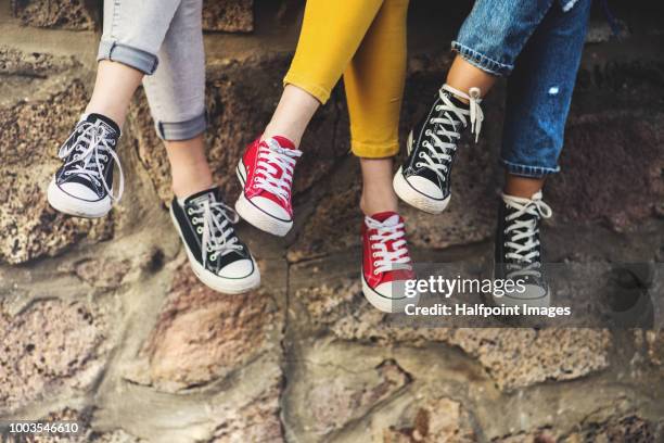 legs of three female teenager friends sitting cross-legged on a wall, wearing sneakers. - girls shoes stock pictures, royalty-free photos & images