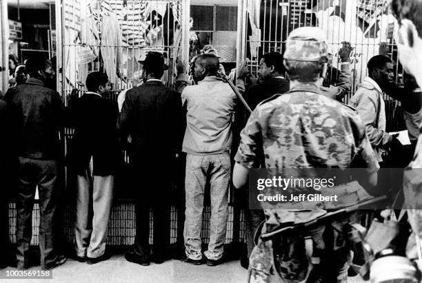 Emeutiers noirs alignés le long d'une grille et surveillés par deux militaires blancs en 1976 à Soweto, Afrique du Sud.