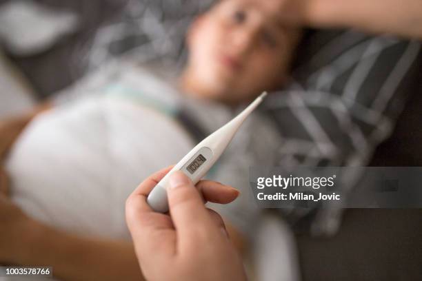 mother checking her sick sons temperature - febre imagens e fotografias de stock