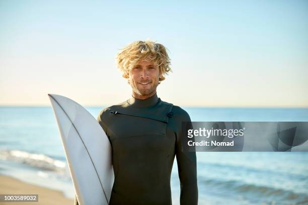 porträt von zuversichtlich mann mit surfbrett am strand - surfer stock-fotos und bilder