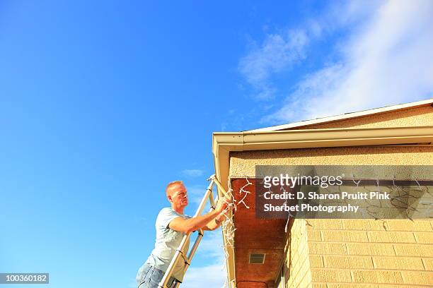 man hanging holiday lights on house with blue sky - utah house stock pictures, royalty-free photos & images