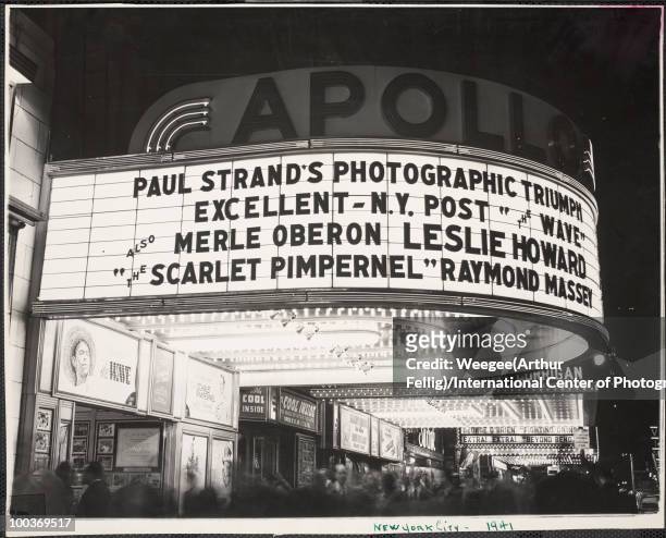 The marquee for the Apollo Theater lit up at night with a crowd milling about outside the theater, located in Times Square, New York, 1941. The...
