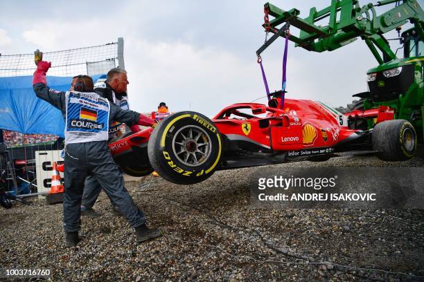 Staff members help as a tractor lifts the car of Ferrari's German driver Sebastian Vettel during the German Formula One Grand Prix at the Hockenheim...