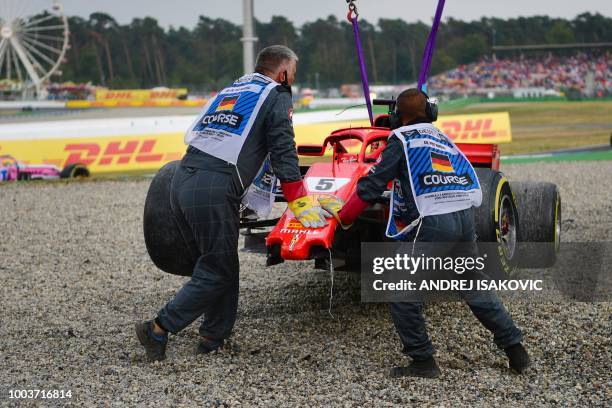 Staff members help as a tractor lifts the car of Ferrari's German driver Sebastian Vettel during the German Formula One Grand Prix at the Hockenheim...