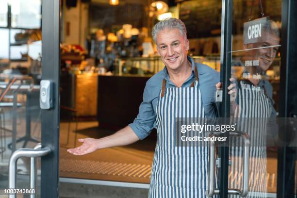 dueño de negocio en la puerta de un café de bienvenida a los clientes - saudar fotografías e imágenes de stock