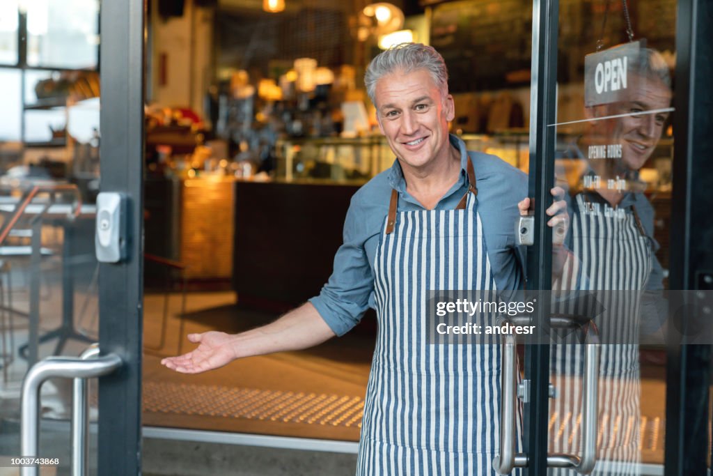 De eigenaar van het bedrijf aan de deur van een café welkom heten van klanten