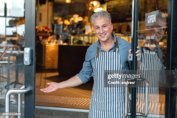 business owner at the door of a cafe welcoming customers - hi imagens e fotografias de stock