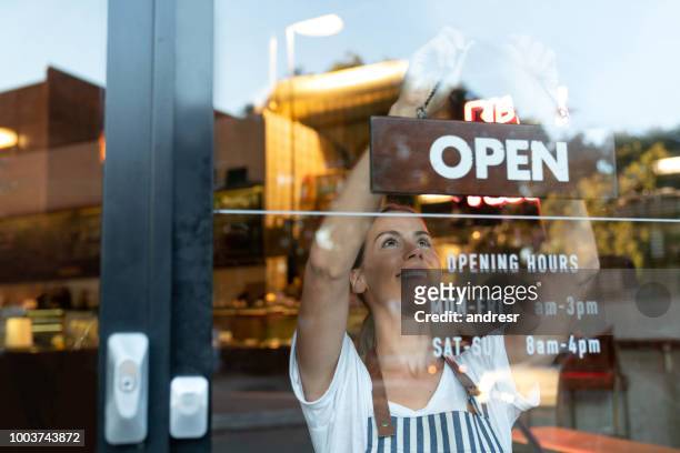 happy business owner hanging an open sign at a cafe - small business stock pictures, royalty-free photos & images