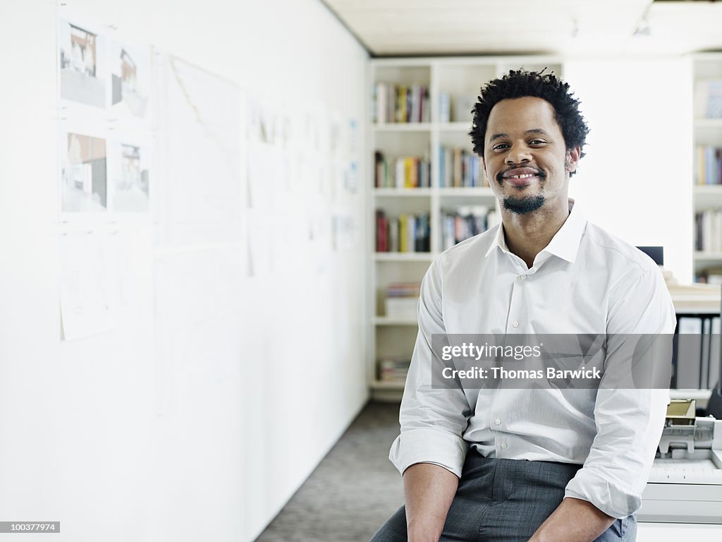 Businessman sitting on edge of desk in office