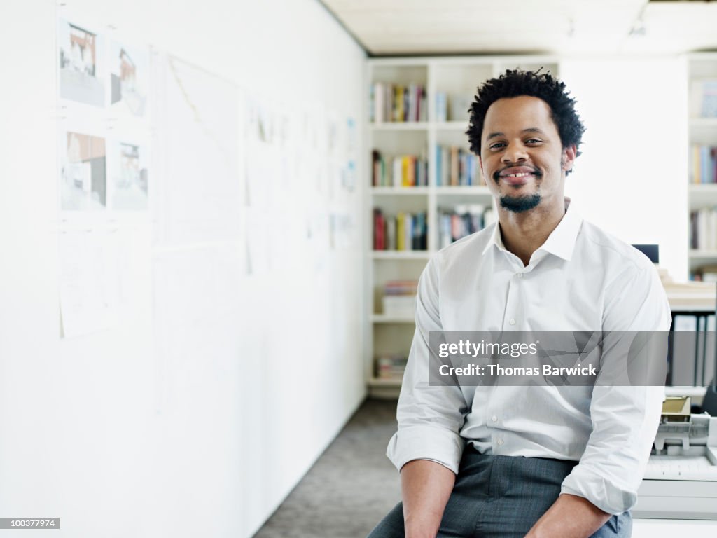 Businessman sitting on edge of desk in office