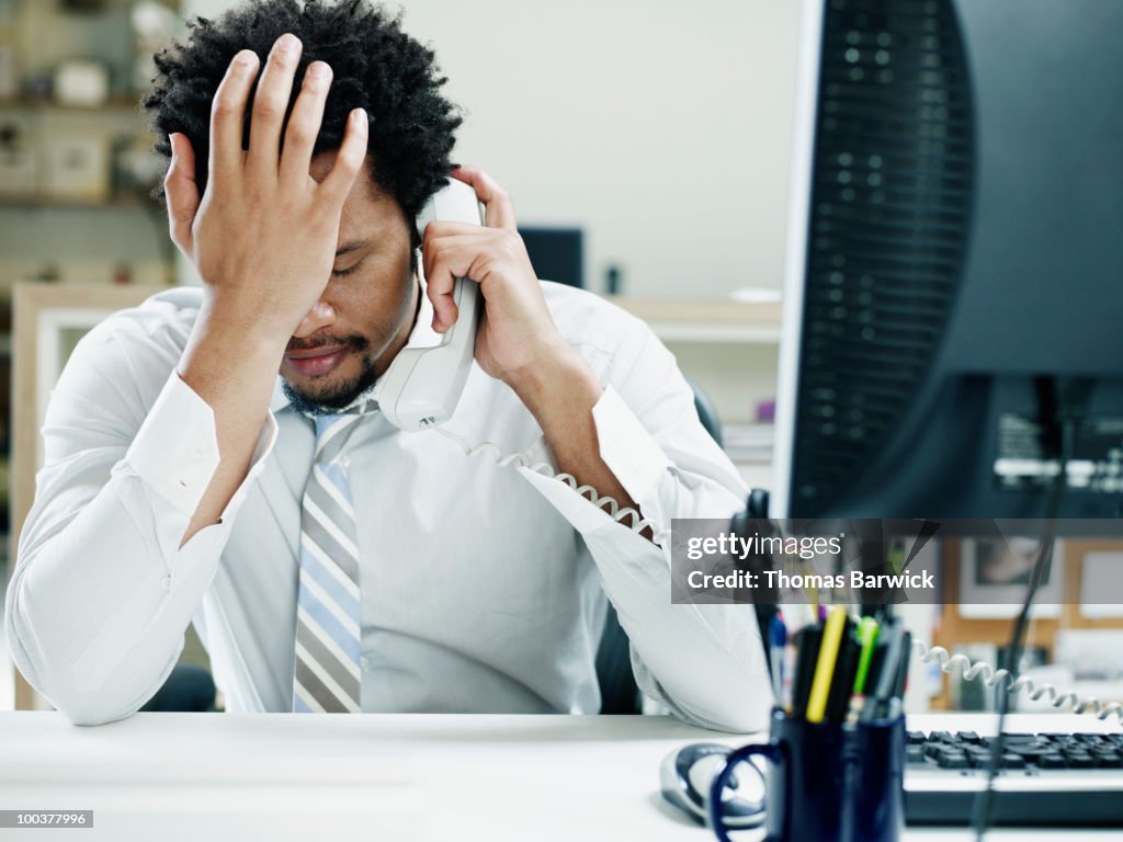 Businessman on phone at desk hand on forehead