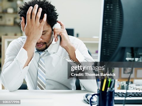 Businessman on phone at desk hand on forehead Businessman on phone at desk hand on forehead