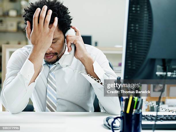 businessman on phone at desk hand on forehead - displeased 個照片及圖片檔