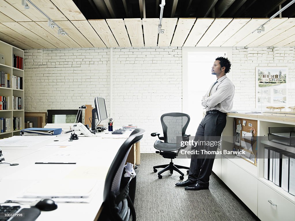 Architect leaning on bookcase in office