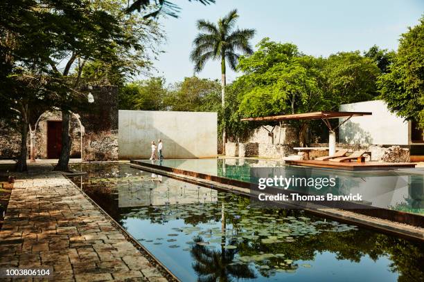 senior couple holding hands while walking by pool on grounds of luxury tropical resort - travel experience stock-fotos und bilder