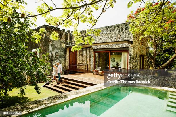senior couple holding hands and walking down steps outside of bungalow at luxury tropical resort - mooi oud stockfoto's en -beelden