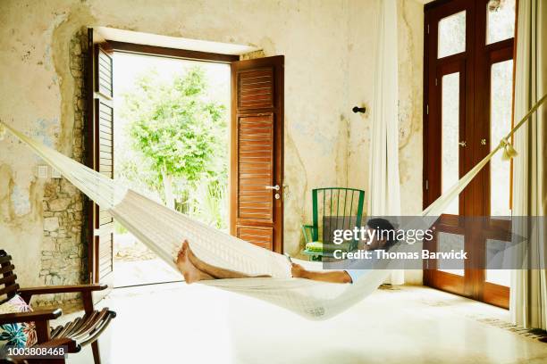 smiling man relaxing in hammock in room at luxury resort reading digital tablet - man ipad holiday stockfoto's en -beelden