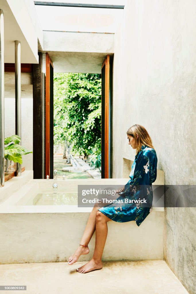 Woman in bathrobe sitting at edge of bathtub